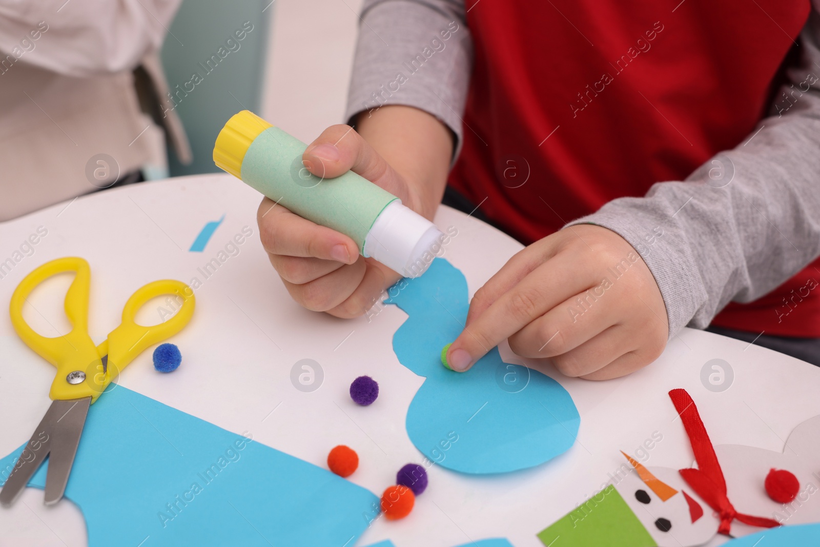 Photo of Little child making Christmas craft at white table, closeup
