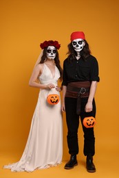 Photo of Couple in scary bride and pirate costumes with pumpkin buckets on orange background. Halloween celebration