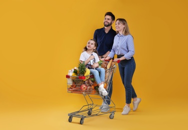 Photo of Happy family with shopping cart full of groceries on yellow background