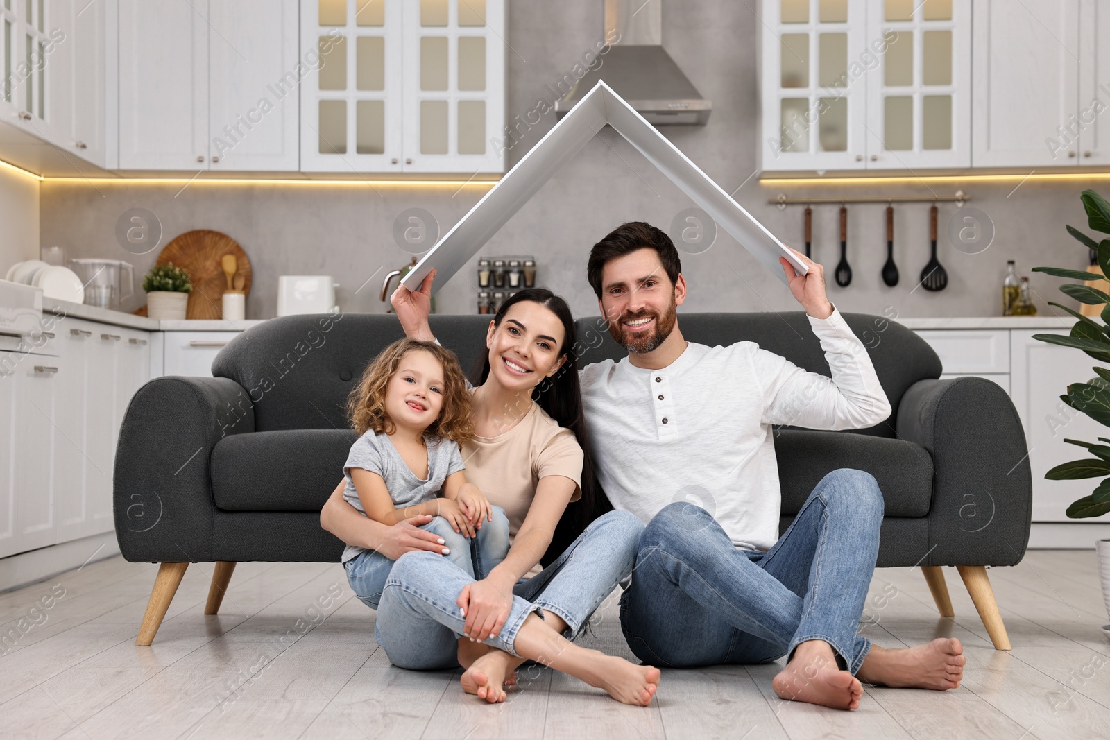 Photo of Housing concept. Happy husband holding plastic roof over his family while sitting on floor at home