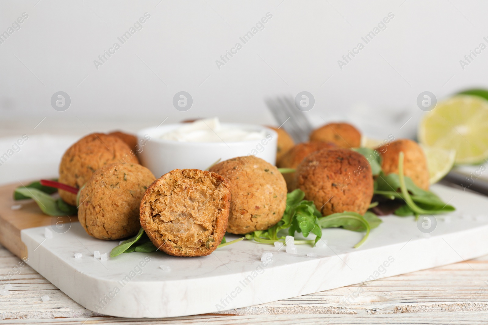 Photo of Delicious falafel balls with herbs, lime and sauce on wooden table, closeup