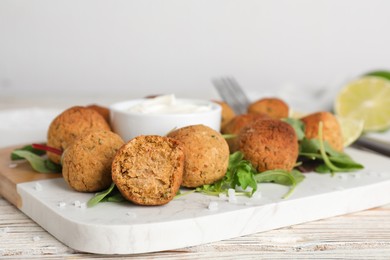 Delicious falafel balls with herbs, lime and sauce on wooden table, closeup