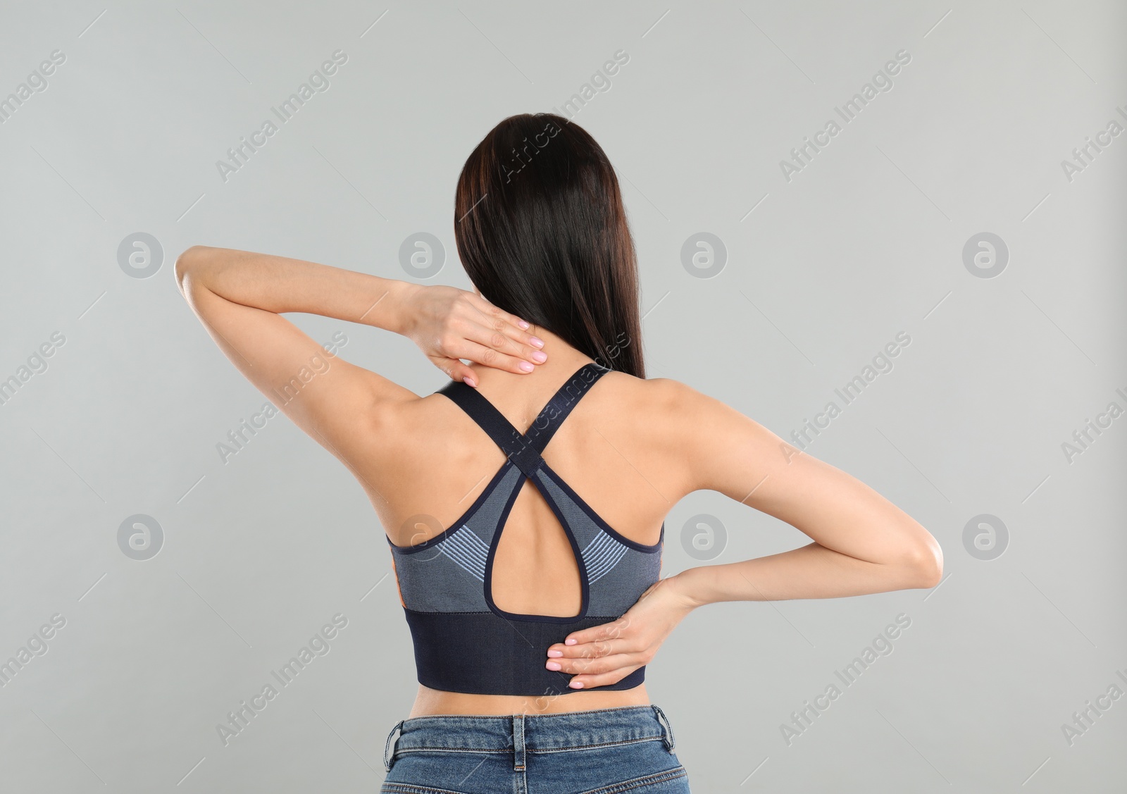 Photo of Woman suffering from pain in back on light grey background. Visiting orthopedist