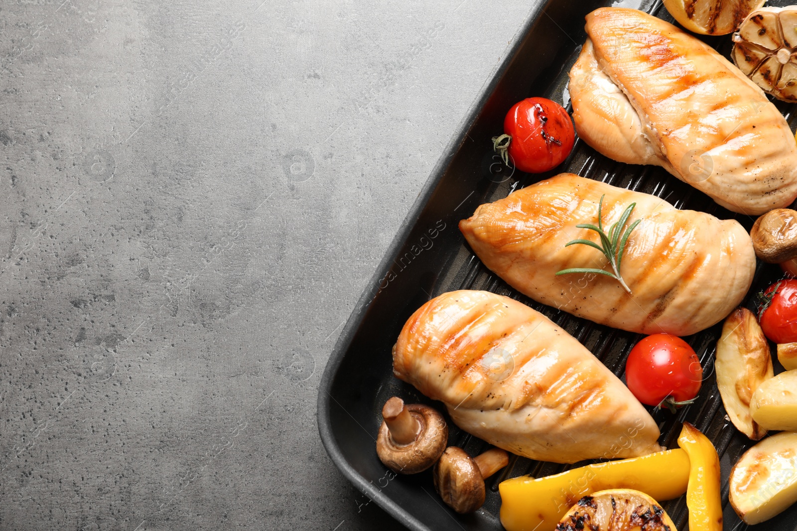 Photo of Grill pan with fried chicken breasts and garnish on grey background, top view. Space for text