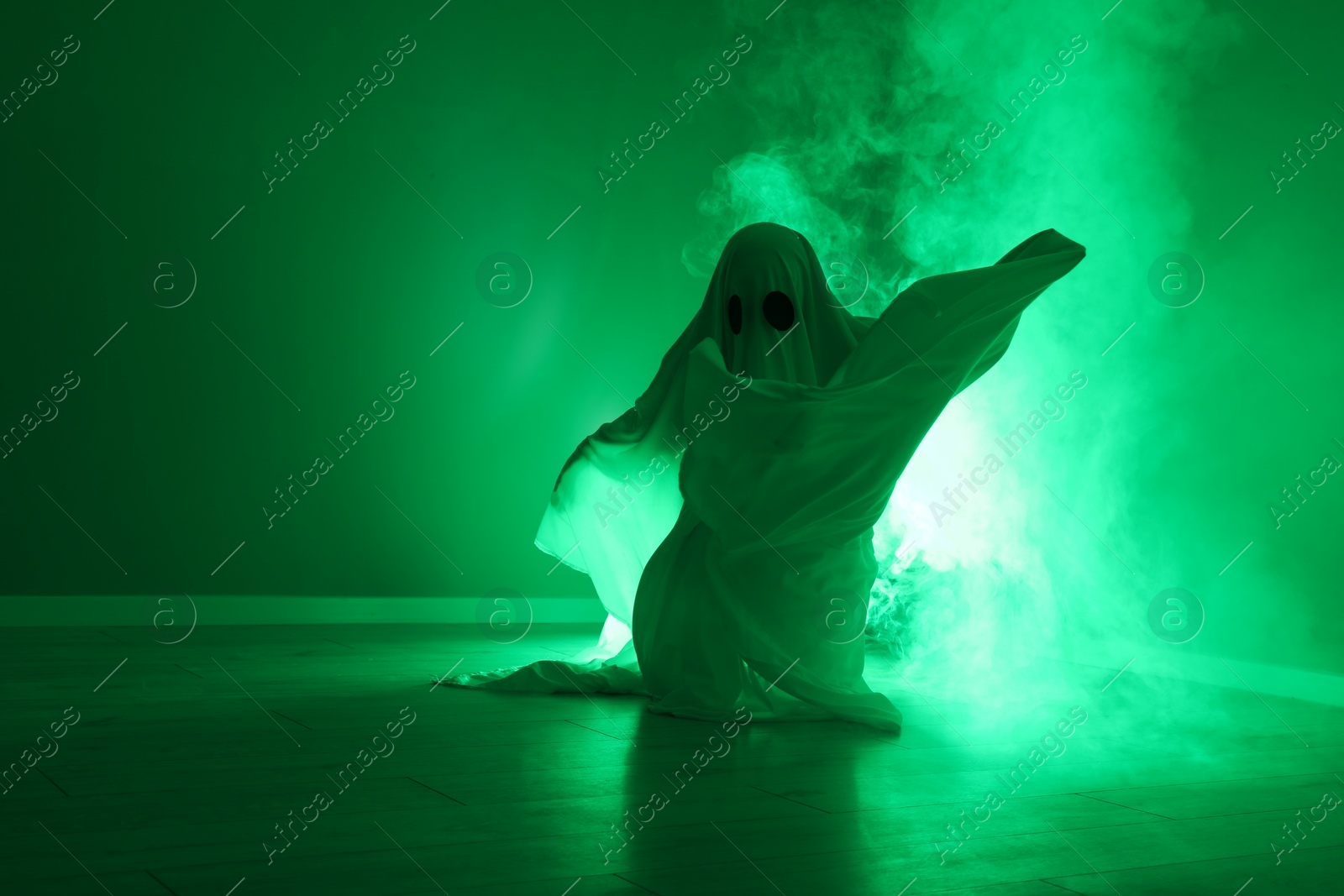 Photo of Creepy ghost. Woman covered with sheet in green light