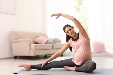 Photo of Young pregnant woman in fitness clothes practicing yoga at home. Space for text