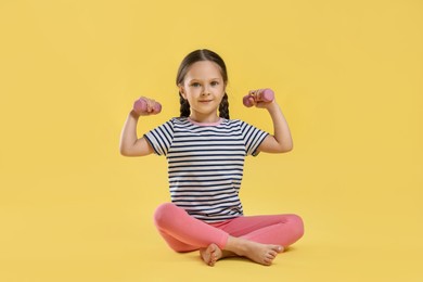 Photo of Cute little girl with dumbbells on yellow background