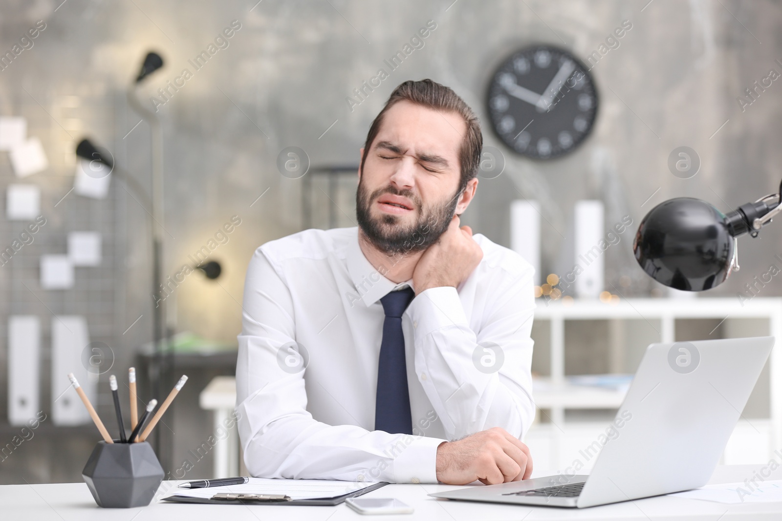 Photo of Young man suffering from neck pain in office