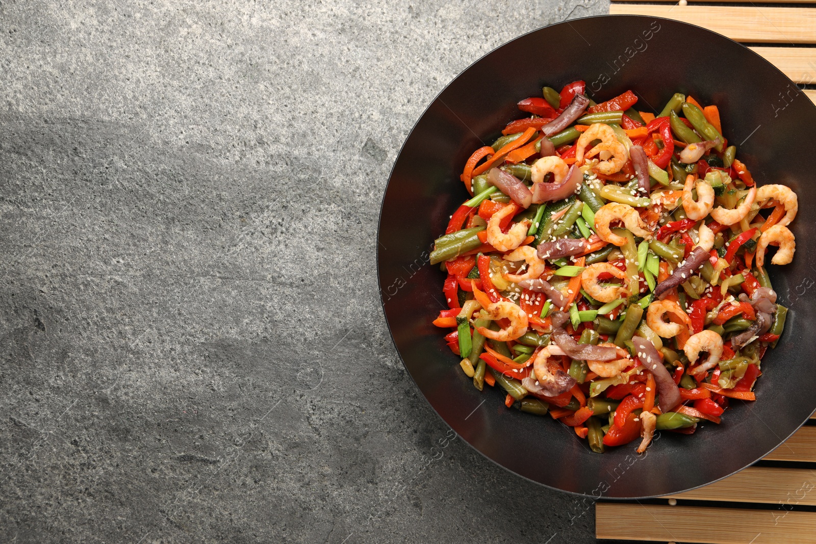 Photo of Shrimp stir fry with vegetables in wok on grey table, top view. Space for text