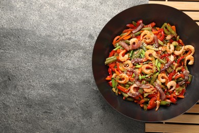 Shrimp stir fry with vegetables in wok on grey table, top view. Space for text