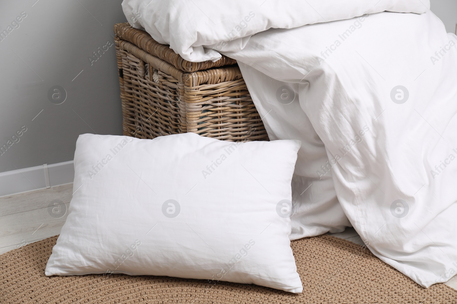 Photo of Soft pillows, duvet and wicker trunk near grey wall indoors