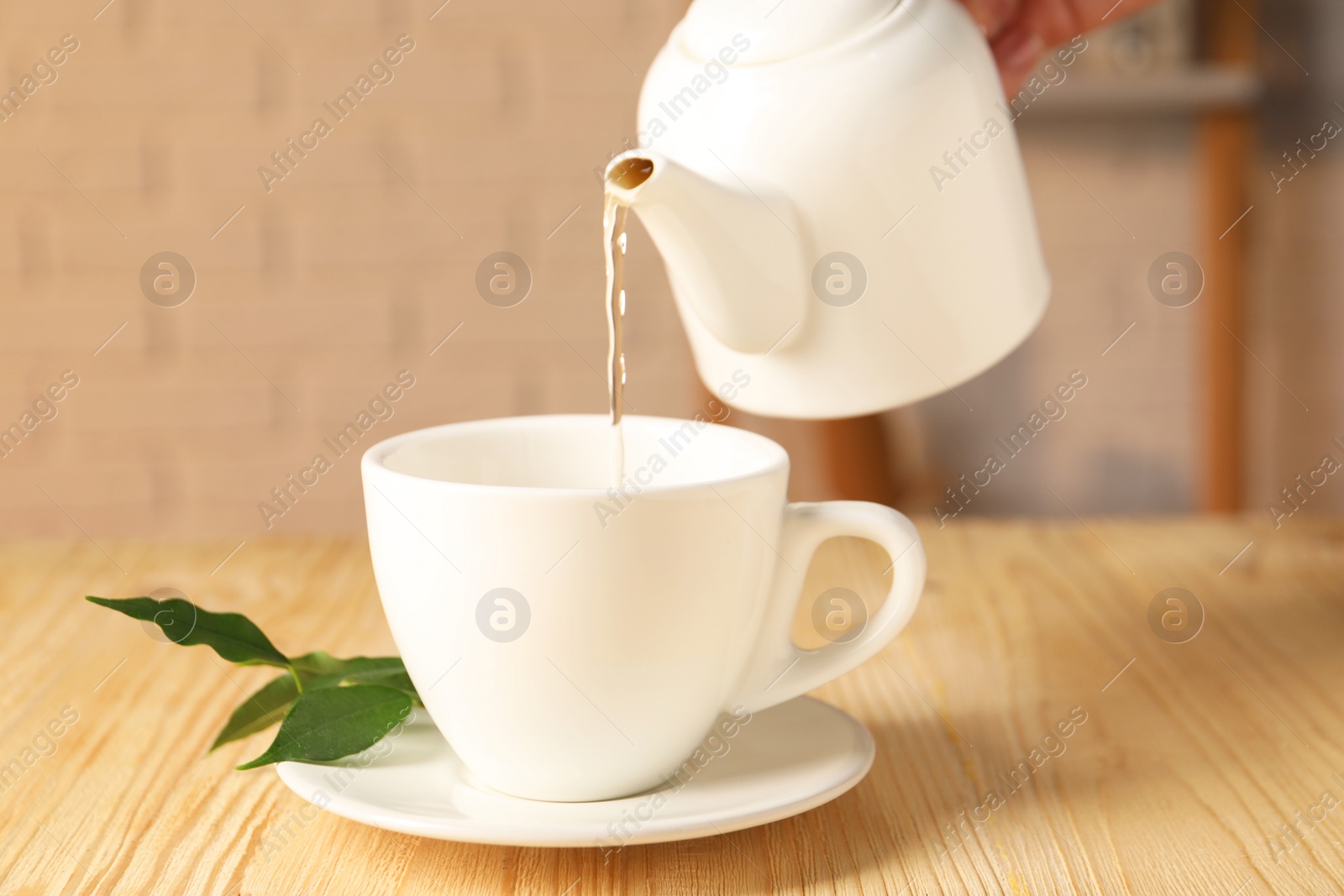 Photo of Pouring tasty tea into cup at light wooden table, closeup