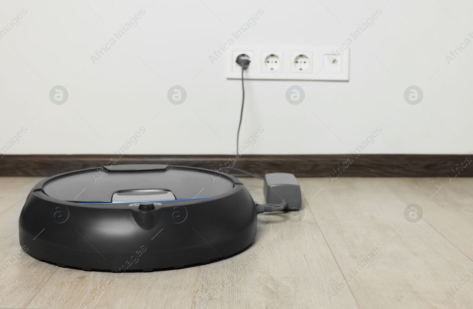 Photo of Robotic vacuum cleaner charging on wooden floor near white wall, space for text