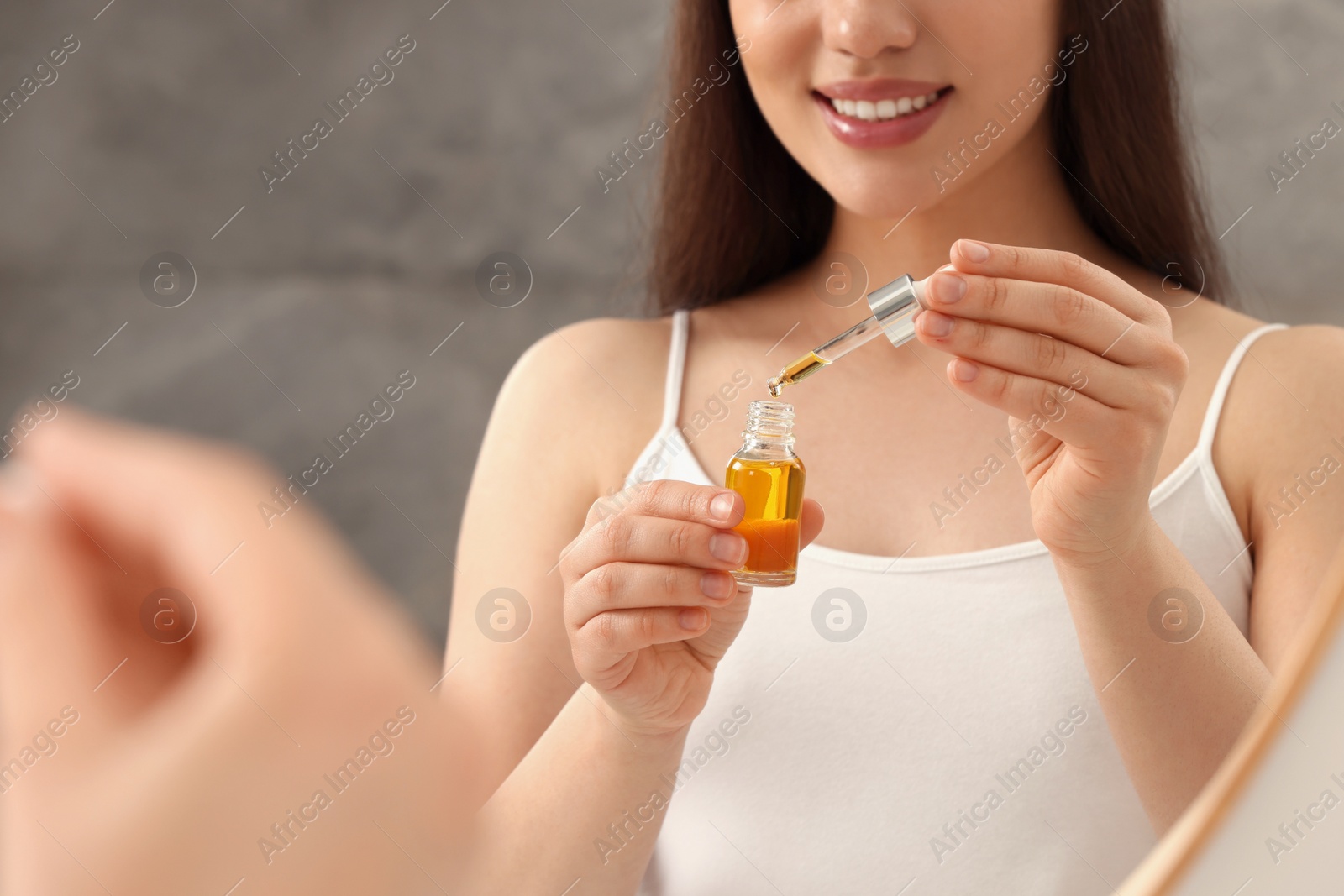 Photo of Woman with bottle of essential oil on blurred background, closeup