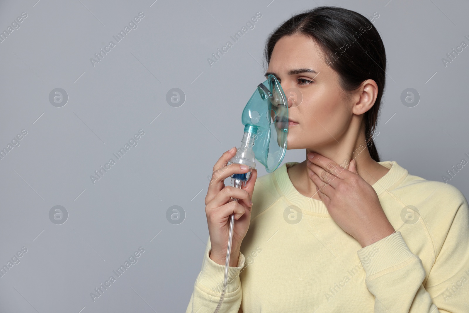 Photo of Sick young woman using nebulizer on grey background, space for text