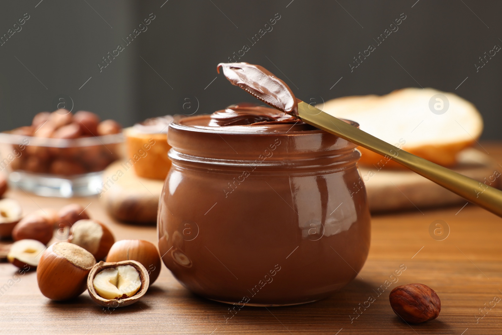 Photo of Glass jar with tasty chocolate hazelnut spread and nuts on wooden table