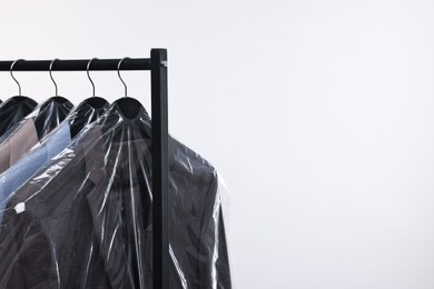 Dry-cleaning service. Many different clothes in plastic bags hanging on rack against white background, space for text