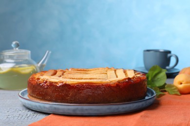 Photo of Tasty apricot pie on grey wooden table against light blue background, space for text