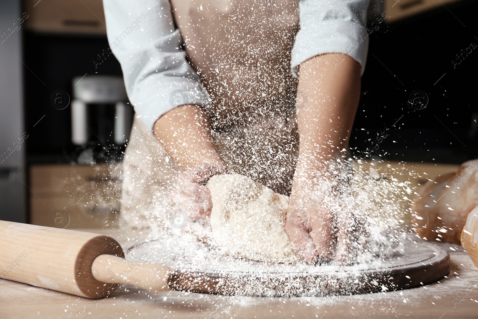 Image of Young woman kneading dough at table in kitchen, closeup