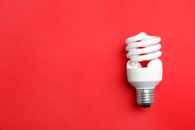 Photo of New fluorescent lamp bulb on red background, top view. Space for text