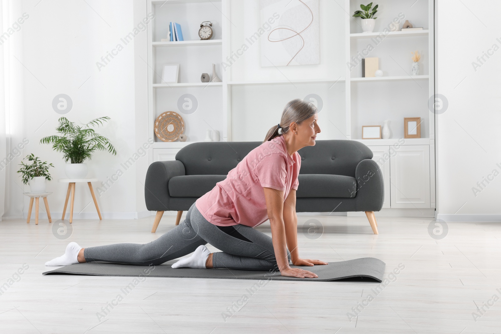 Photo of Senior woman in sportswear stretching on fitness mat at home