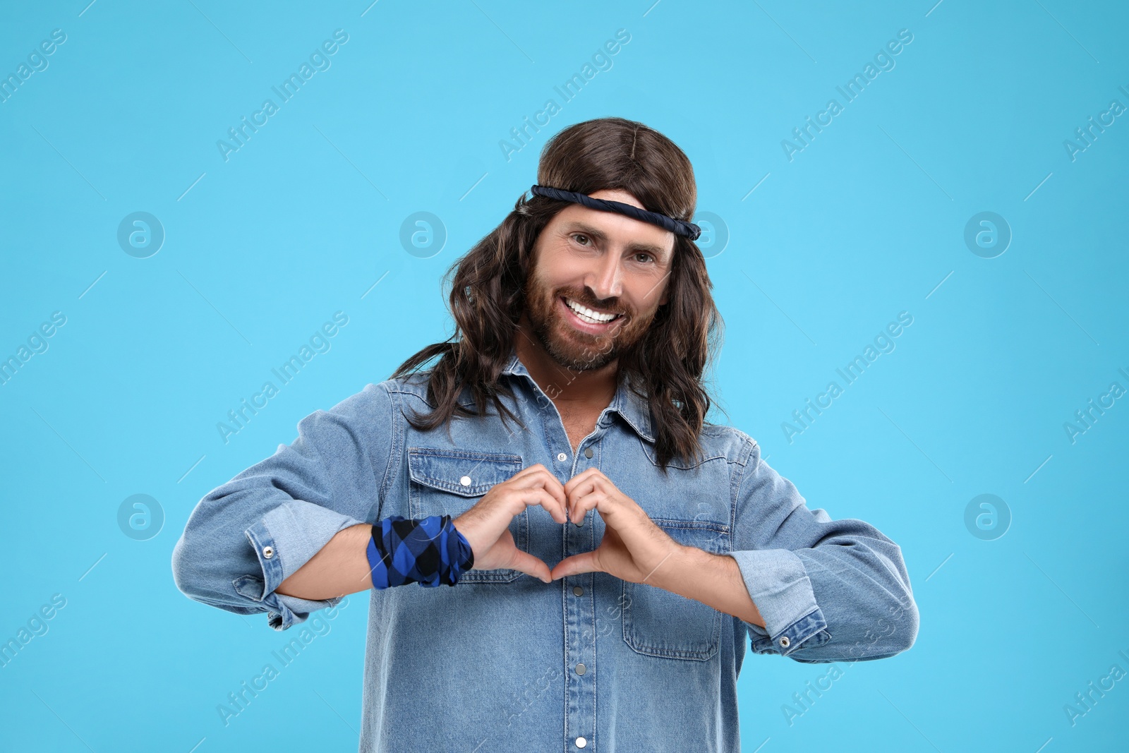 Photo of Stylish hippie man making heart with hands on light blue background