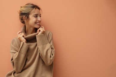 Beautiful young woman wearing knitted sweater on light brown background. Space for text