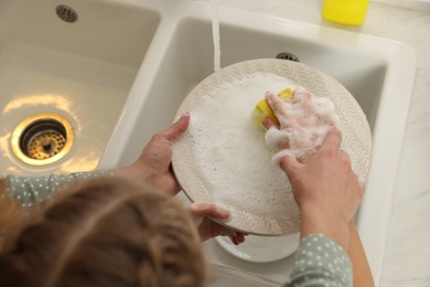 Photo of Mother and daughter washing plate in sink, above view