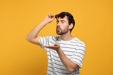 Photo of Handsome man blowing kiss on orange background