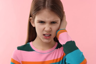 Hearing problem. Little girl suffering from ear pain on pink background