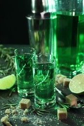 Photo of Absinthe in shot glasses, spoon, brown sugar, lime and rosemary on gray table, closeup. Alcoholic drink