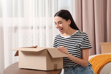 Photo of Emotional young woman opening parcel at home. Internet shopping