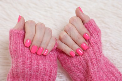 Woman showing her manicured hands with pink nail polish on faux fur mat, closeup