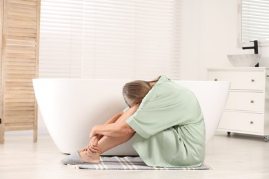 Photo of Menopause. Depressed woman near bath tub in bathroom