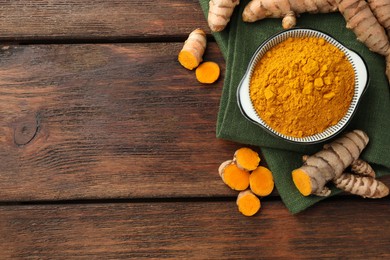 Photo of Bowl with aromatic turmeric powder and cut roots on wooden table, flat lay. Space for text