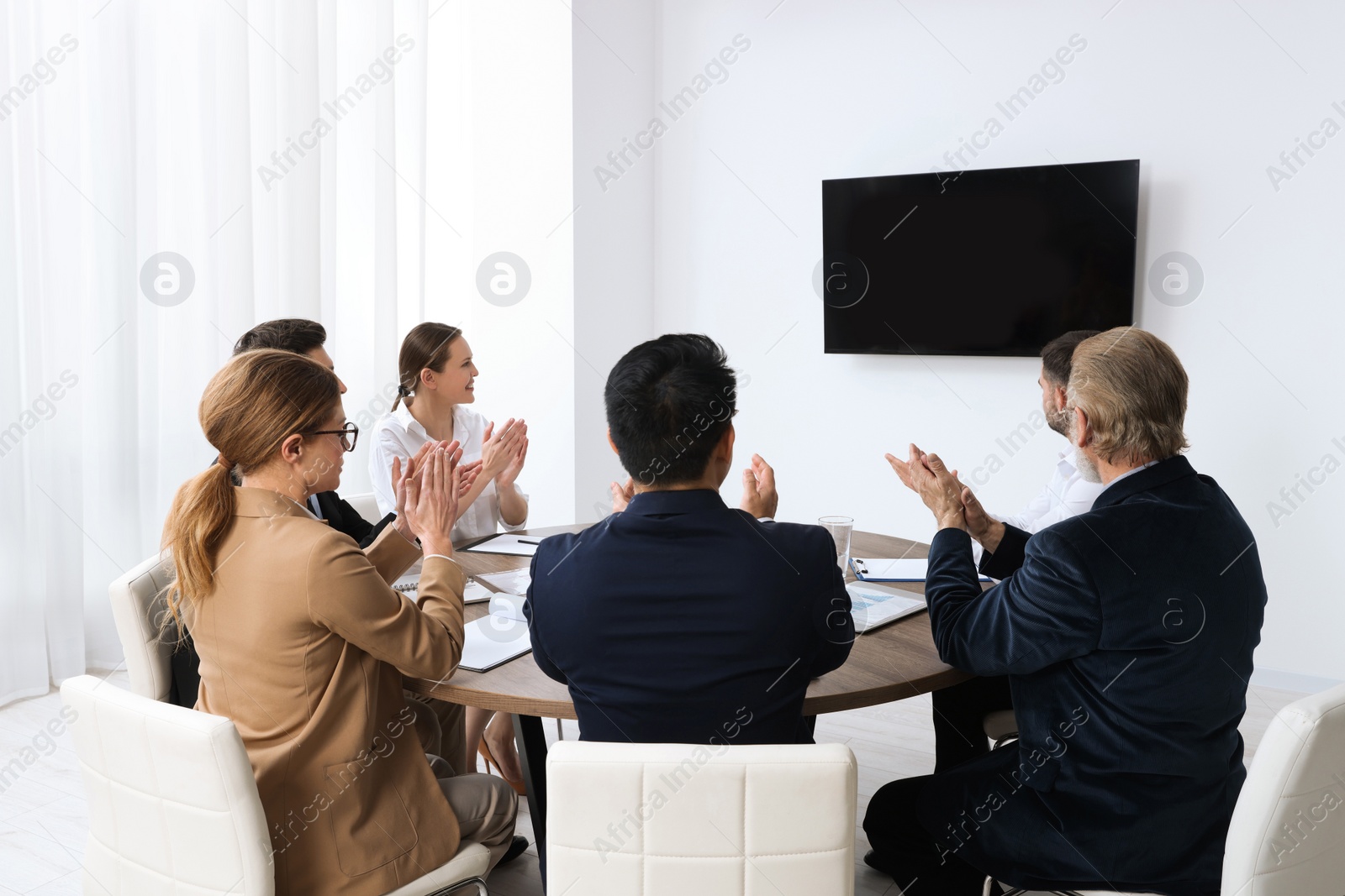 Photo of Business conference. Group of people watching presentation on tv screen in meeting room
