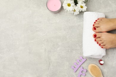 Photo of Woman with stylish red toenails after pedicure procedure, tools and chamomile flowers on grey textured background, top view. Space for text