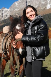 Photo of Young woman stroking horse in mountains on sunny day. Beautiful pet