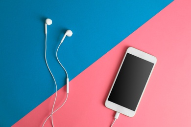 Photo of Modern phone with earphones on color background, top view. Space for text