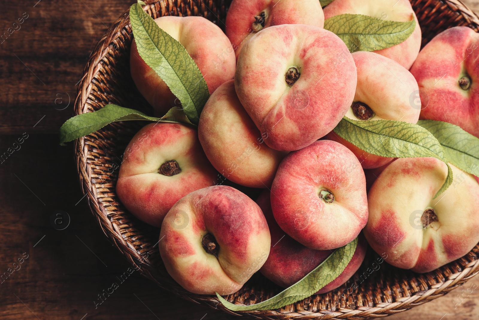 Photo of Fresh ripe donut peaches in basket on wooden table, top view