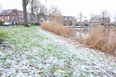 Picturesque view of canal, buildings and grass covered with snow in city on winter day