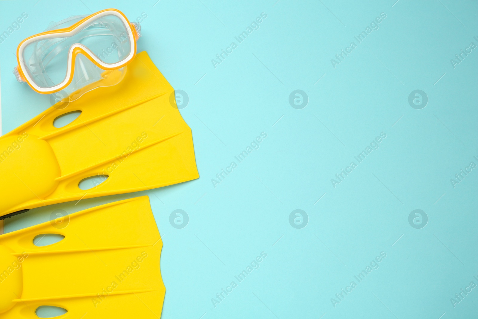 Photo of Pair of yellow flippers and diving mask on turquoise background, flat lay