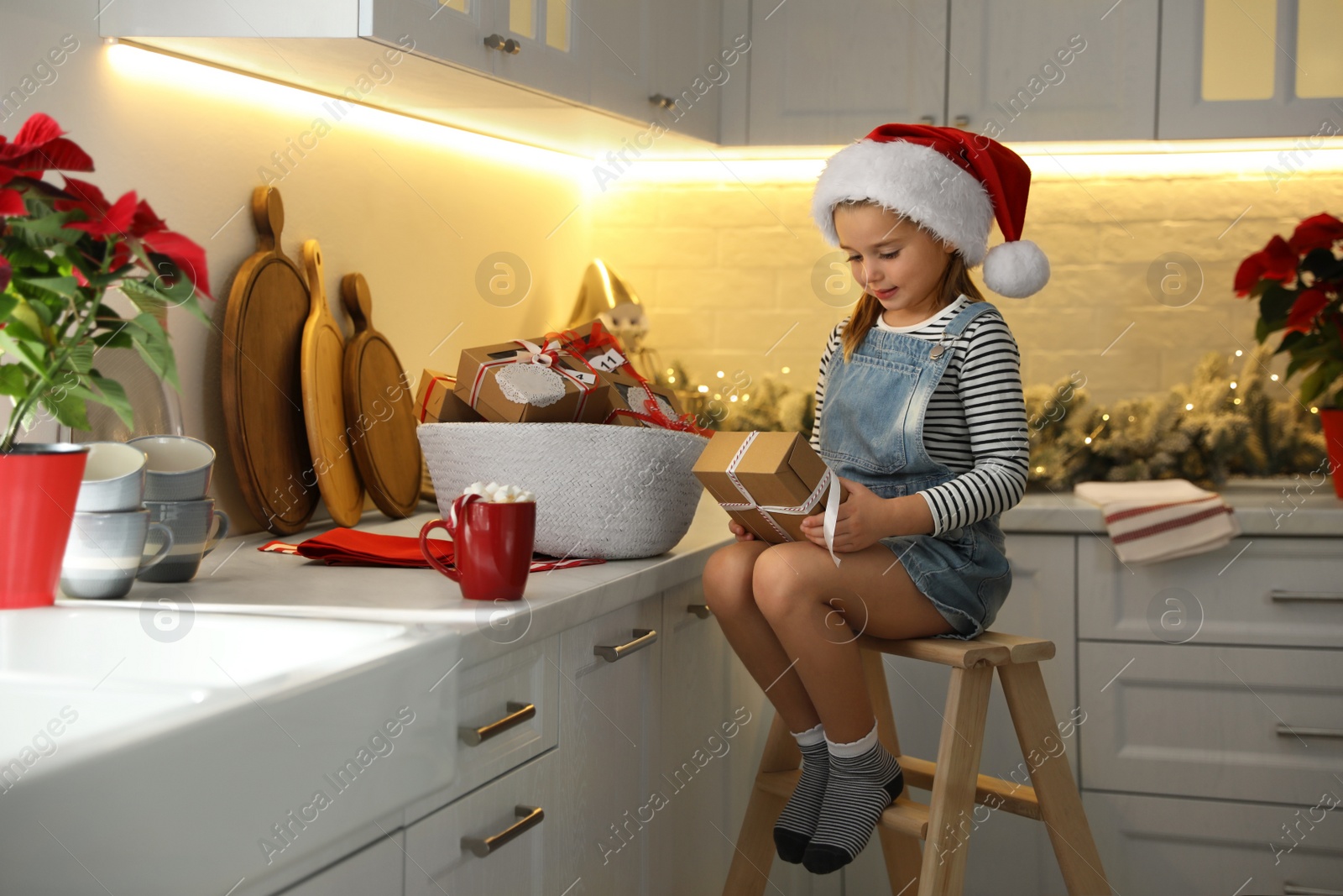 Photo of Cute little girl in Santa hat with gift from Christmas advent calendar at home