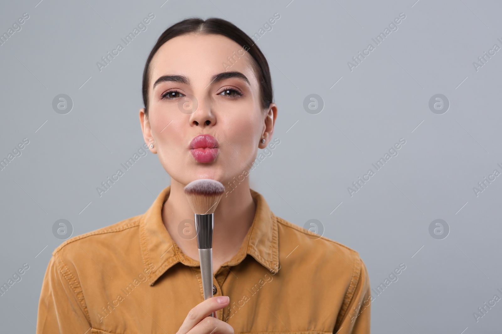 Photo of Woman with makeup brush on light grey background, space for text