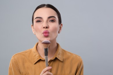 Woman with makeup brush on light grey background, space for text