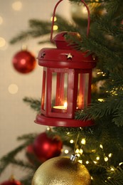 Christmas lantern with burning candle on fir tree against blurred background, closeup