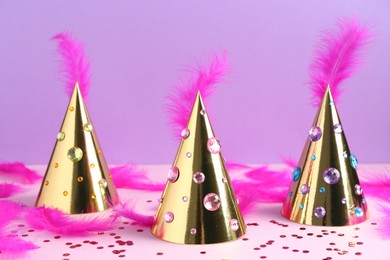 Photo of Golden party hats with bright feathers, rhinestones and confetti on color background