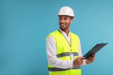 Photo of Engineer in hard hat holding clipboard on light blue background, space for text