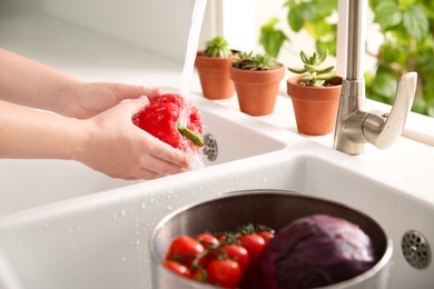 Woman washing fresh bell pepper in kitchen sink, closeup