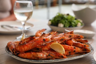 Photo of Plate of delicious cooked shrimps served with lemon and wine at table outdoors, closeup